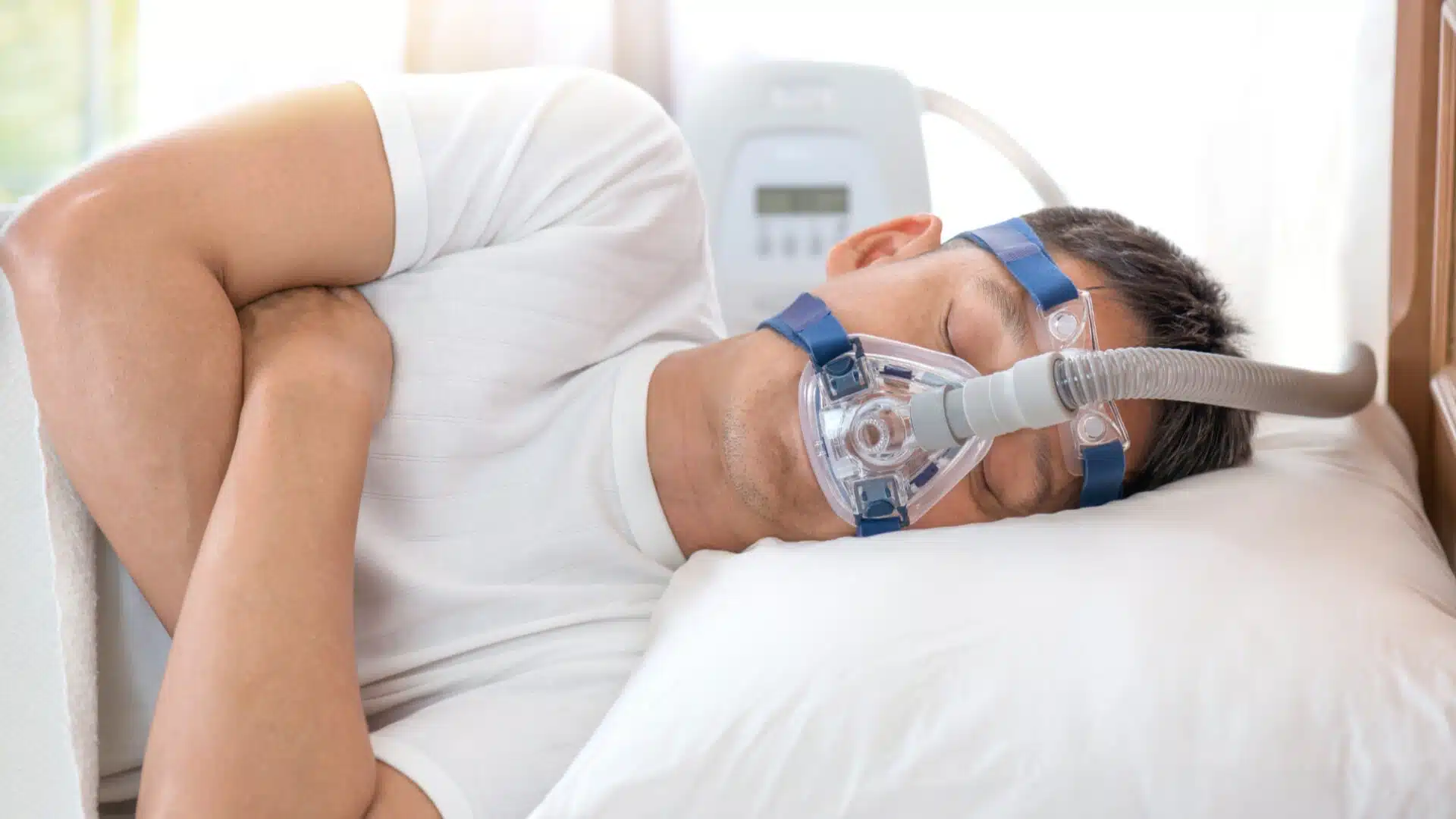Health Hub 85 Middle-aged man wearing CPAP mask while sleeping on his side, using continuous positive airway pressure therapy machine to treat obstructive sleep apnea and improve nighttime breathing