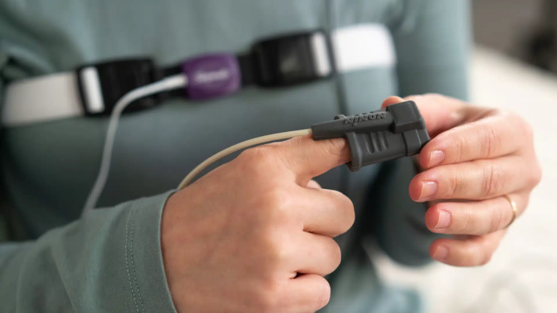 Health Hub 83 Close-up of person using home sleep apnea test device with finger pulse oximeter sensor and chest belt to monitor breathing during sleep study