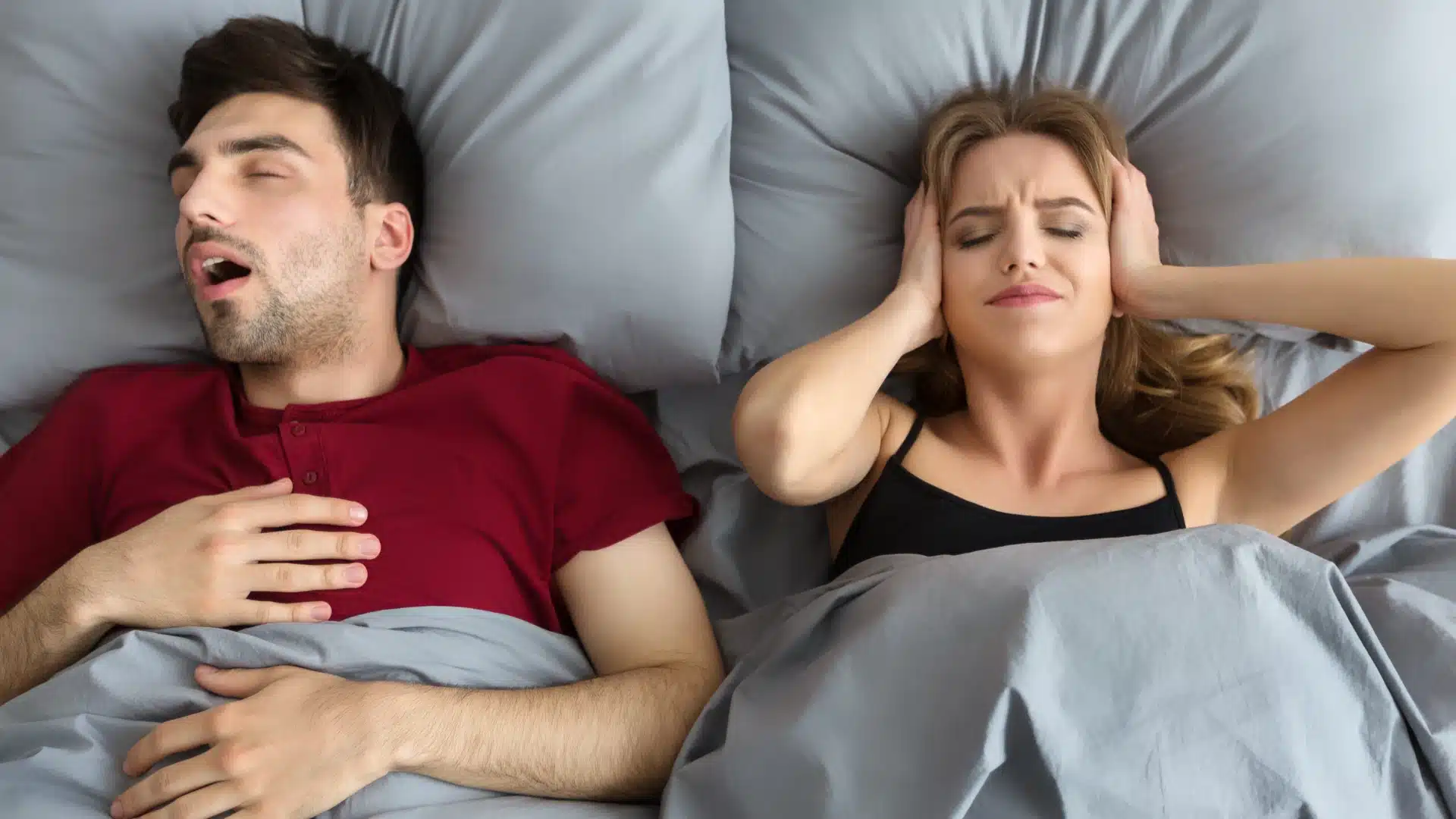 Health Hub 17 Woman covering ears in bed while man snores loudly beside her at night