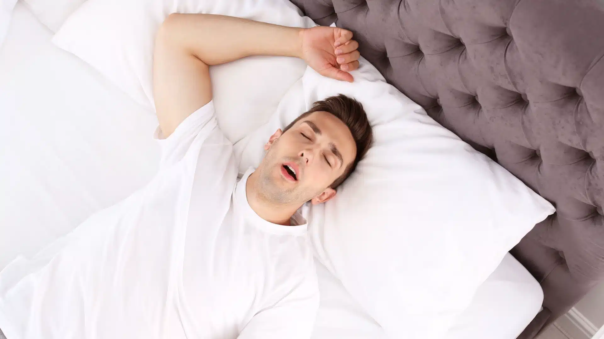 Health Hub 34 Young man sleeping on his back with mouth open, showing common symptom of sleep apnea and snoring, potential breathing issues during sleep