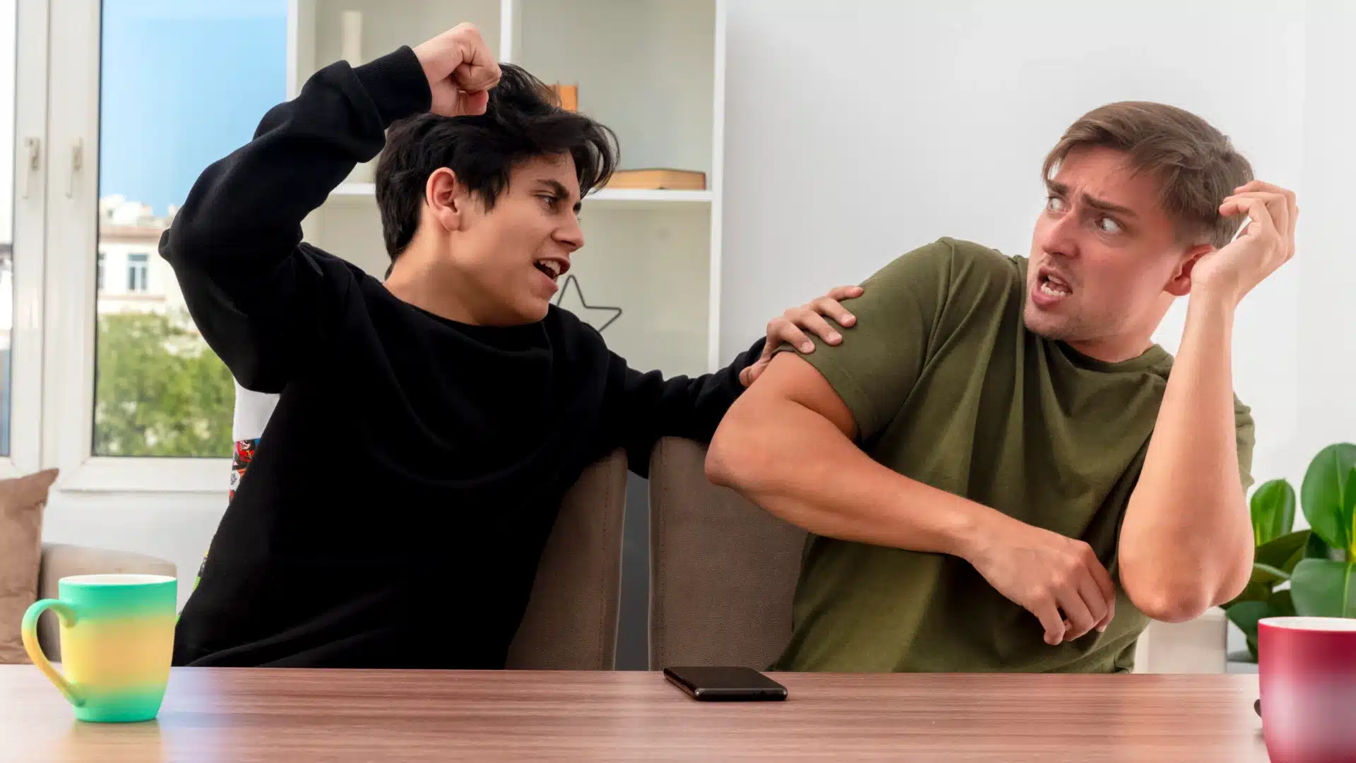Health Hub 18 Two young men arguing at home with one raising fist and the other reacting defensively