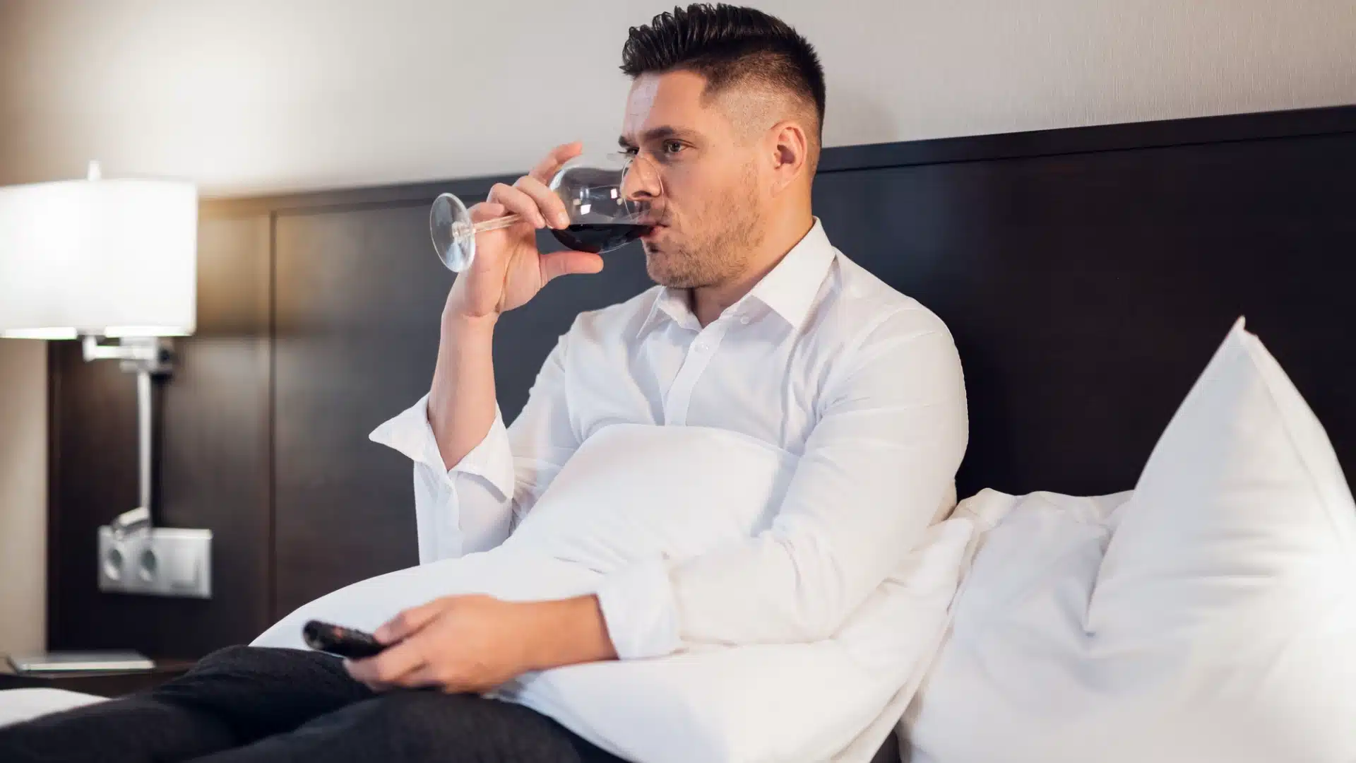 Health Hub 45 Man sitting in bed drinking red wine while watching TV in the evening