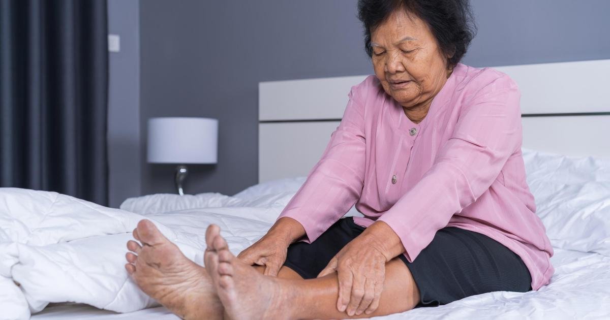 Health Hub 10 Elderly woman sitting on bed massaging swollen legs, suffering from varicose veins and poor circulation