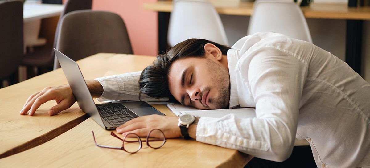 Health Hub 12 Tired man sleeping on desk with laptop open, suffering from workplace fatigue and burnout