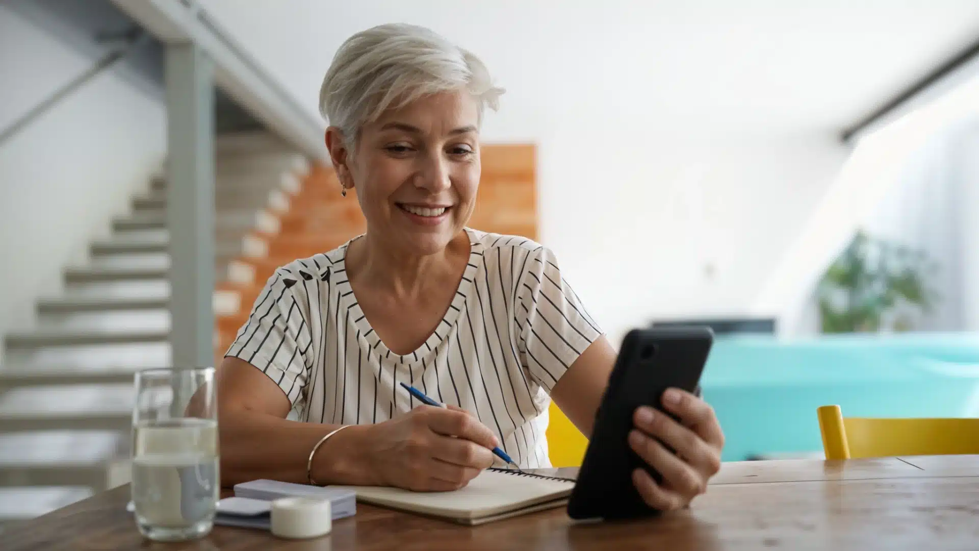 Health Hub 68 Smiling senior woman taking notes while having a video call on smartphone at home