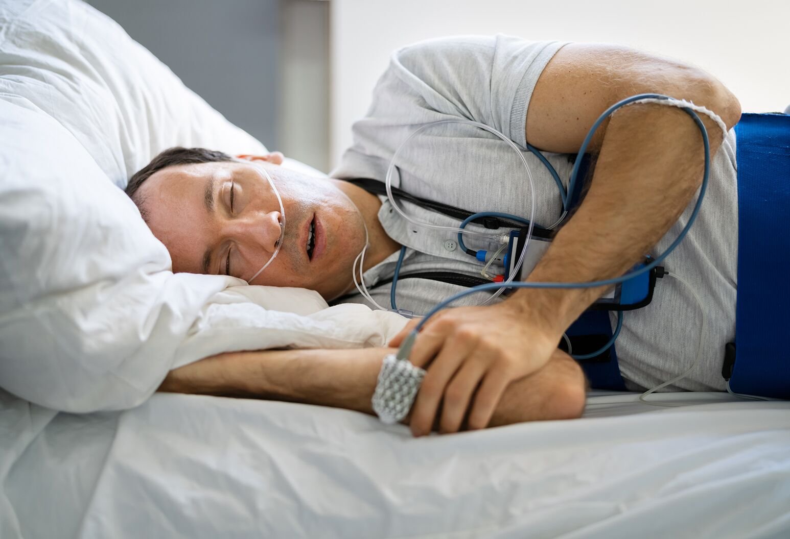 Health Hub 32 Middle-aged man sleeping with nasal cannula and monitoring devices during overnight sleep study for diagnosing sleep apnea and sleep disorders