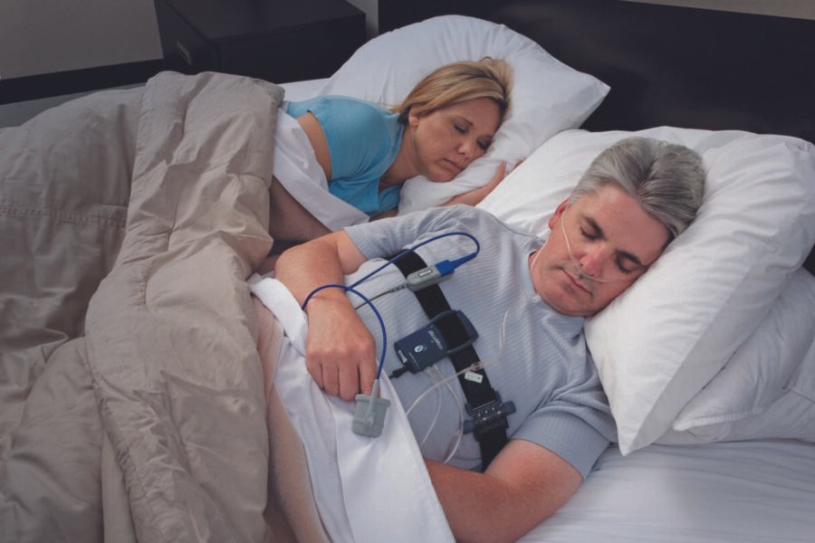 Health Hub 31 Man undergoing sleep apnea test with monitoring equipment while sleeping beside partner