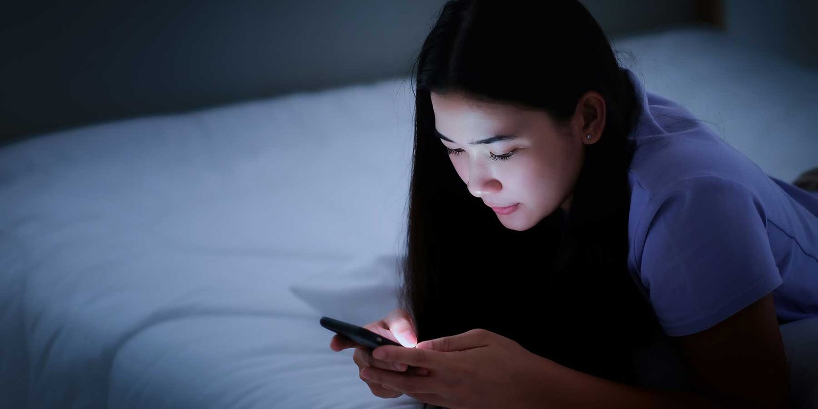 Health Hub 57 Young woman using smartphone in bed at night, blue light affecting sleep quality