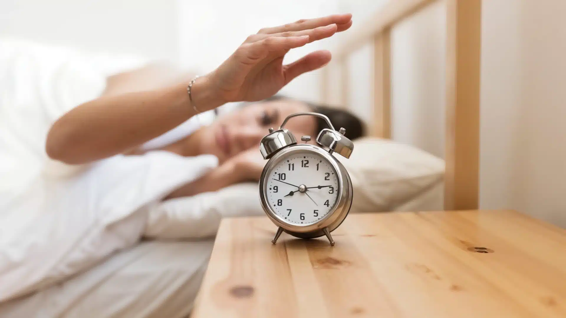 Health Hub 72 Person in bed reaching to turn off alarm clock on wooden nightstand in the morning