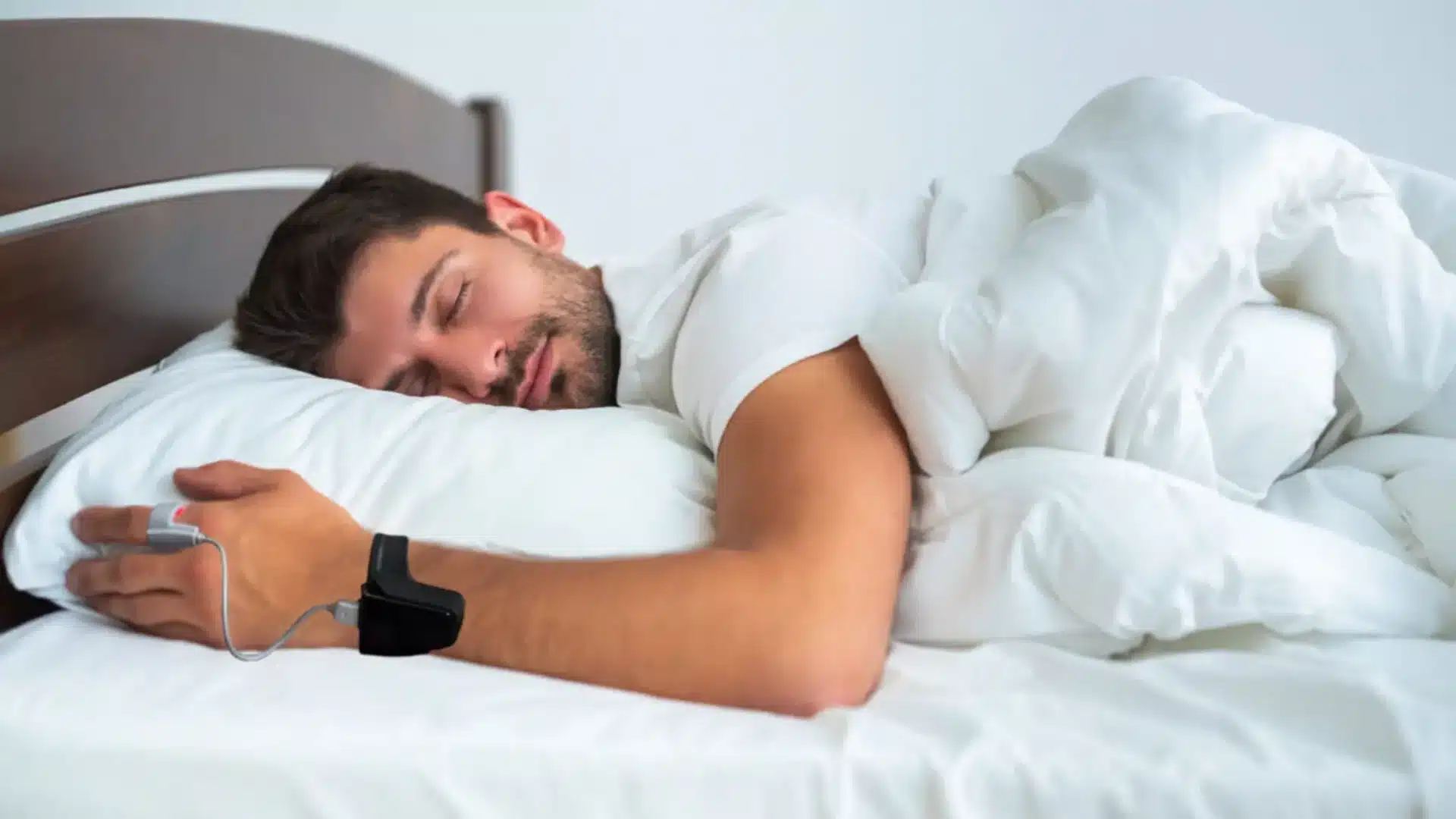 Man sleeping in bed while wearing a sleep Apnea at Home test kit on wrist and finger for overnight oxygen monitoring